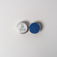 An open aluminum tin of vibrant blue powder on a white background with a white label that says Lakota Made Hazatho Blue Eyeshadow Ingredients blue spirulina powder and arrowroot powder.