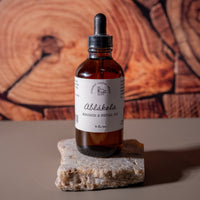 A brown dropper bottle with a white label that says Lakota Made Ablakela Massage and Facial Oil 4 fl. oz. The bottle is on a flat piece of quartz rock on a tan table top in front of a cut wood grain background.