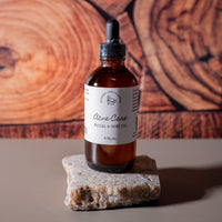 A brown dropper bottle with a white label that says Lakota Made Acne Care Facial & Body Oil 4 flx. oz. The bottle is resting on a flat piece of quartz on a gray table top in front of a wood grain background