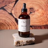 A brown dropper bottle with a white label that says Lakota Made Beard Oil 4 fl. oz. The bottle is on top of a slab of rose quartz with a wood grain background.