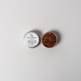 An open aluminum tin or rich brown powder on a white background with a white label that says Lakota Made Brown Goddess Eyeshadow Ingredients mica powder, kaolin clay powder, arrowroot powder.