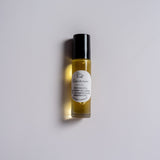 A clear glass roller bottle with a black lid and a white label that says Cinnamon Lip Oil ingredients sunflower oil argan oil cinnamon bark essential oil on a white background.