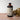 A large brown bottle with a white label that says Lakota Made Elderberry Chaga Tonic. There is a bundle of dried flowers next to the bottle. It is resting on a wooden table top in front of a white background.