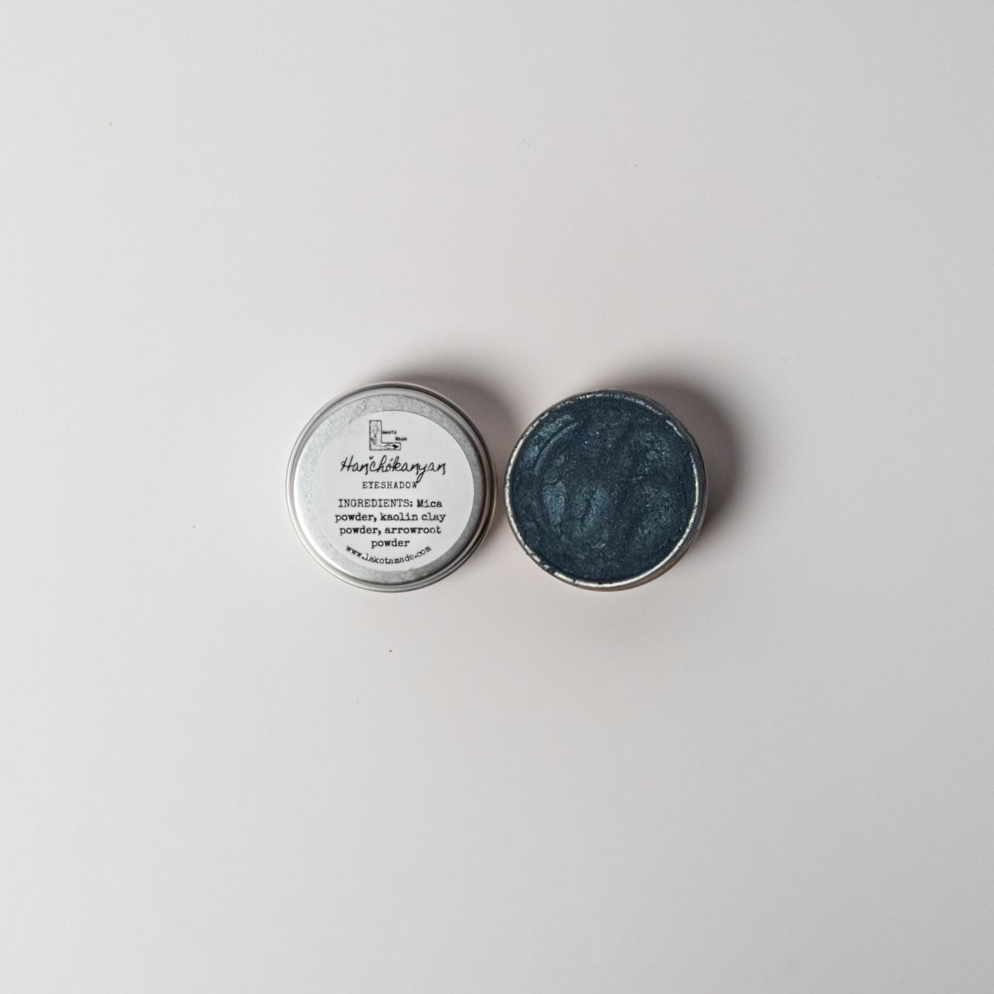 An open aluminum tin of midnight blue powder on a white background with a white label that says Lakota Made BHanchokanyan Dark Blue Eyeshadow Ingredients mica powder, kaolin clay powder, arrowroot powder.