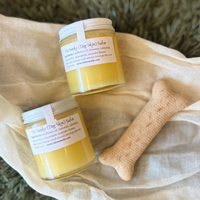 Two glass jars with white lids and labels that say Ha Sunka Dog Skin Salve on a linen towel with a dog bone biscuit