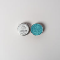 An open aluminum tin of vibrant light blue powder on a white background with a white label that says Lakota Made Makhatho Blue Earth Eyeshadow Ingredients mica powder, kaolin clay powder, arrowroot powder.