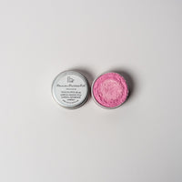 An open aluminum tin or bright pink powder on a white background with a white label that says Lakota Made Powow Princess Pink Eyeshadow Ingredients mica powder, kaolin clay powder, arrowroot powder.