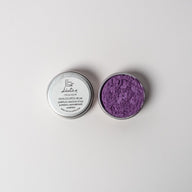 An open aluminum tin of purple powder on a white background with a white label that says Lakota Made Sastan Purple Eyeshadow Ingredients mica powder, kaolin clay powder, arrowroot powder.