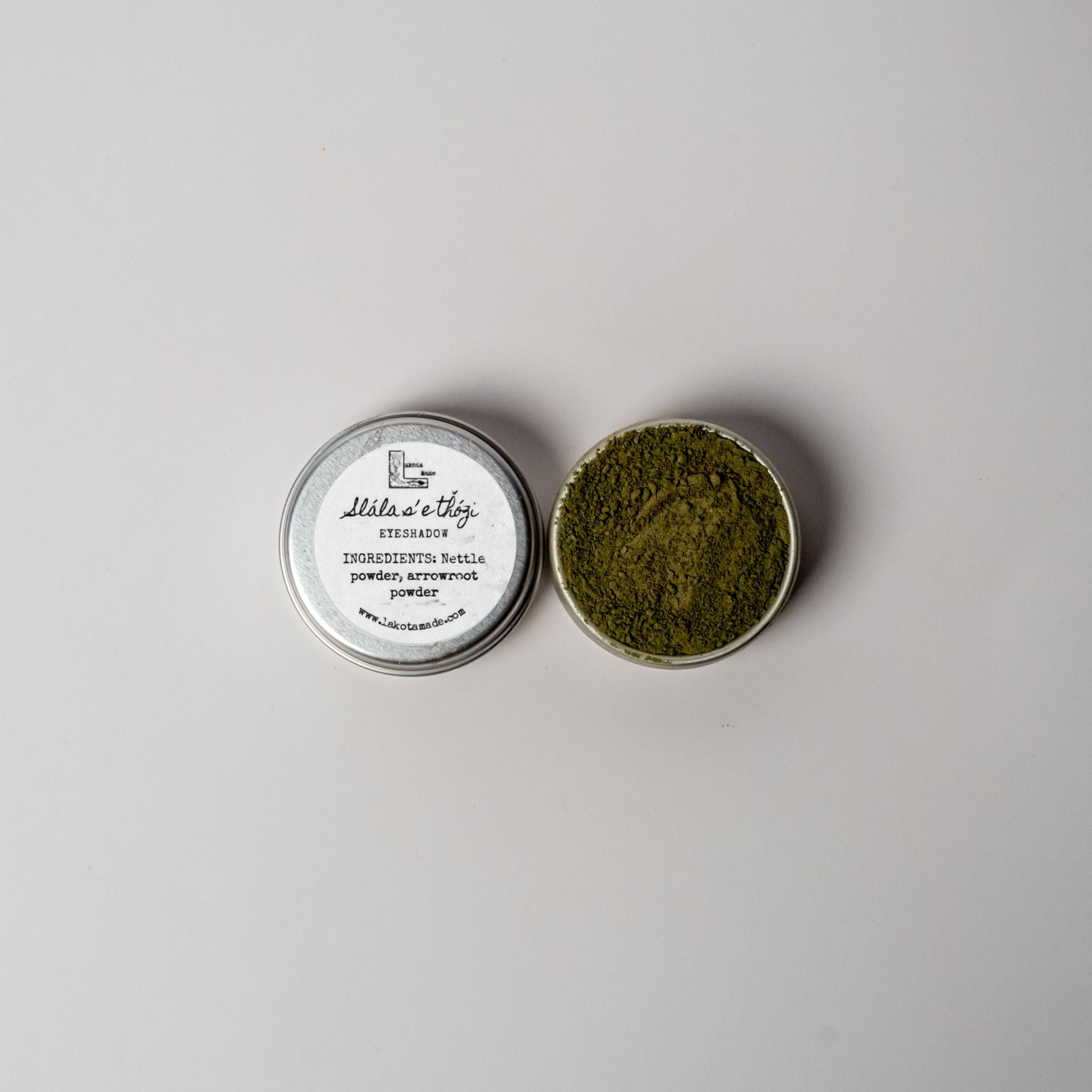 An open aluminum tin of dark olive green powder on a white background with a white label that says Slalase Thozi Dark Green Eyeshadow Ingredients nettle powder, arrowroot powder.