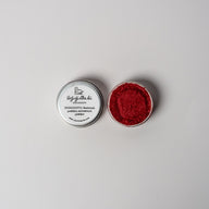 An open aluminum tin of vibrant red powder on a white background with a white label that says Lakota Made Unzizintka Hu Wild Rose Eyeshadow Ingredients alfalfa powder, arrowroot powder.