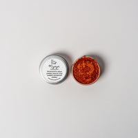 An open aluminum tin of vibrant copper orange powder on a white background with a white label that says Lakota Made Wiyaya Eyeshadow Ingredients mica powder, kaolin clay powder, arrowroot powder.