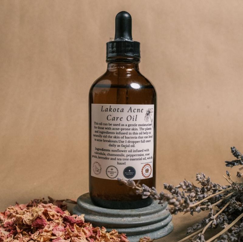 Brown dropper bottle with a white label that says Lakota Acne Care Oil surrounded by dried flowers and lavender