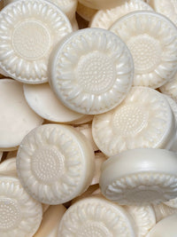 A close up image of round flower shaped cream colored soap bars in a pile. 